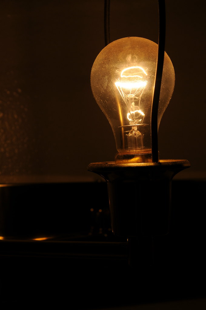 A glowing filament light bulb lit against a dark background